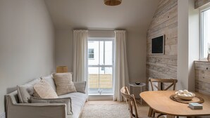Una habitación acogedora con techo de madera, un sofá con cojines, una mesa de comedor con sillas y una lámpara colgante.