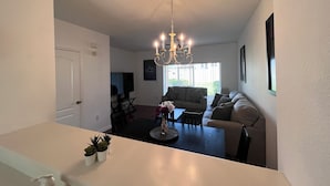 Un salon moderne avec un lustre, un canapé, une table basse et un coin repas.