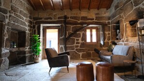 A rustic stone interior with wooden beams, two leather armchairs, a small round ottoman, and a potted plant. - JADS Guesthouse (Montalegre)