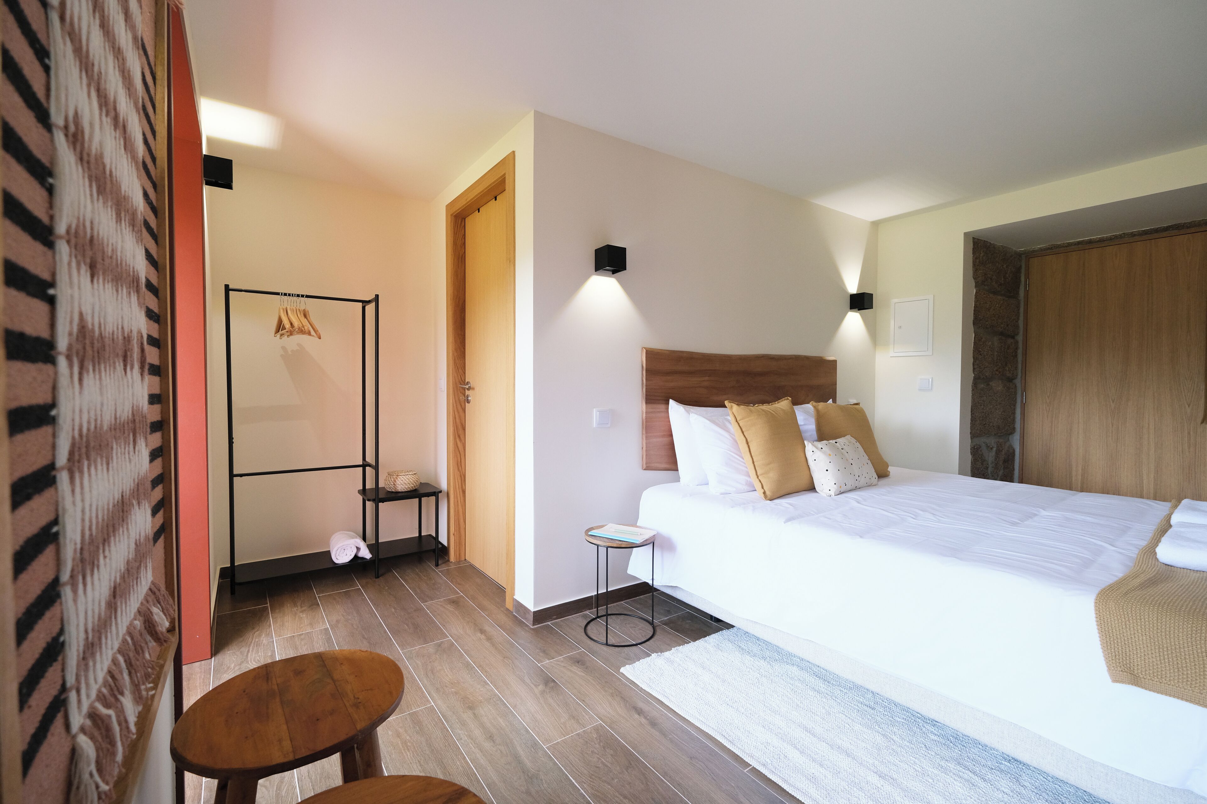 A hotel room with a large bed, a small bedside table, a wall-mounted shelf, and a wooden floor.