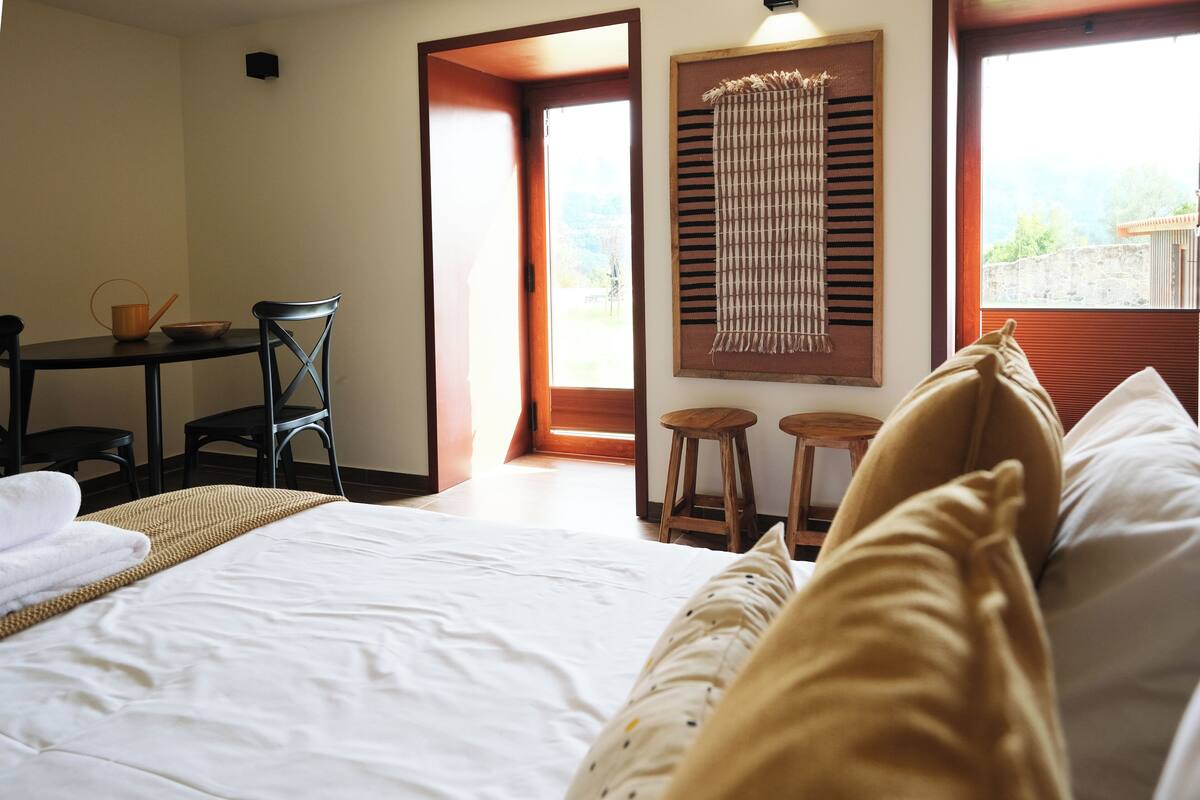 Una camera d'albergo con un letto, un tavolo da pranzo con sedie, uno sgabello e una finestra vista.