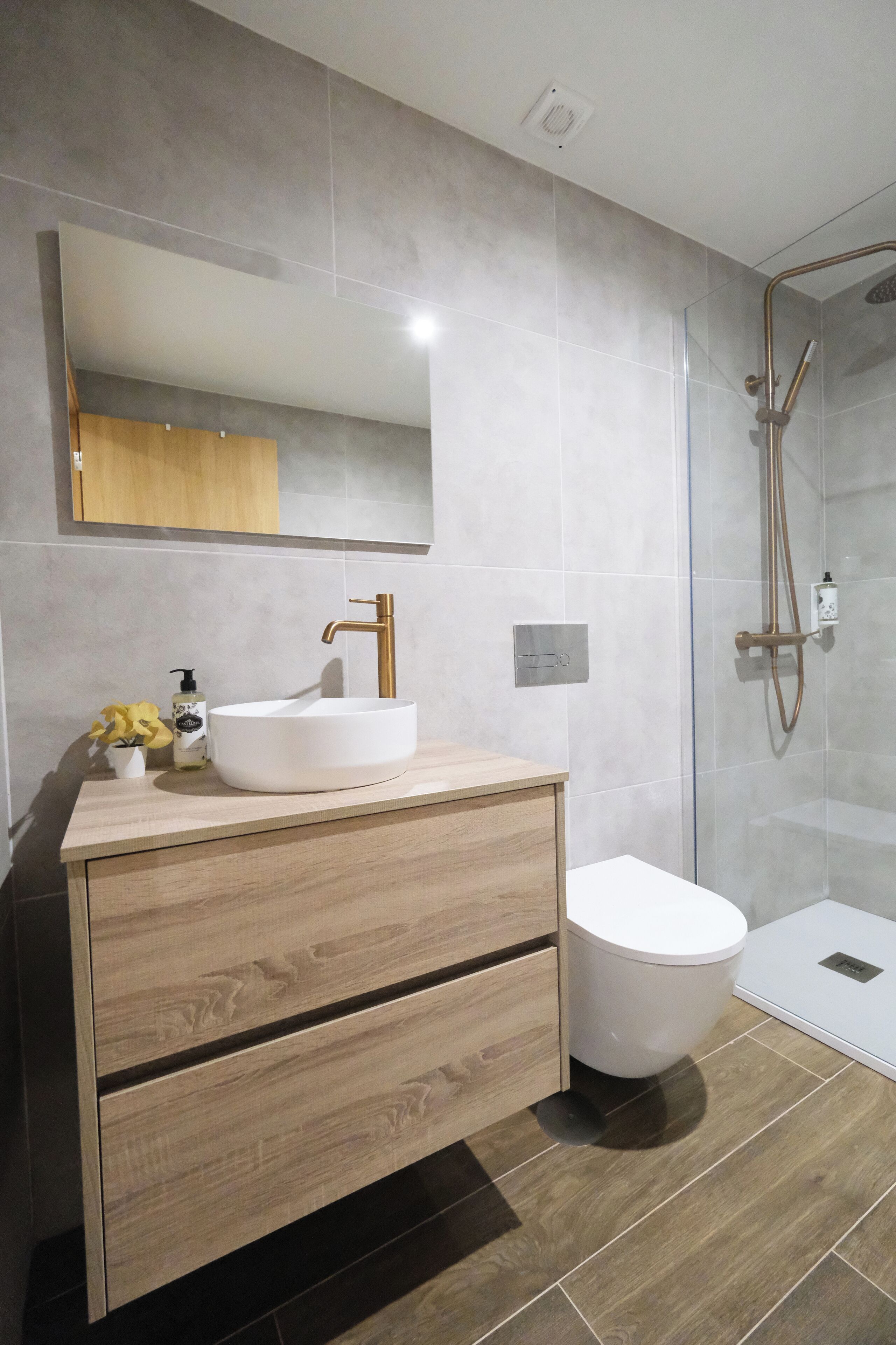 A modern bathroom with a wooden vanity, white sink, and a glass shower enclosure.