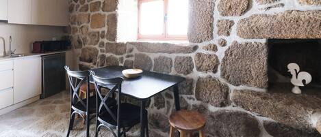 Une cuisine aux murs de pierre, avec une fenêtre, une table et deux chaises.