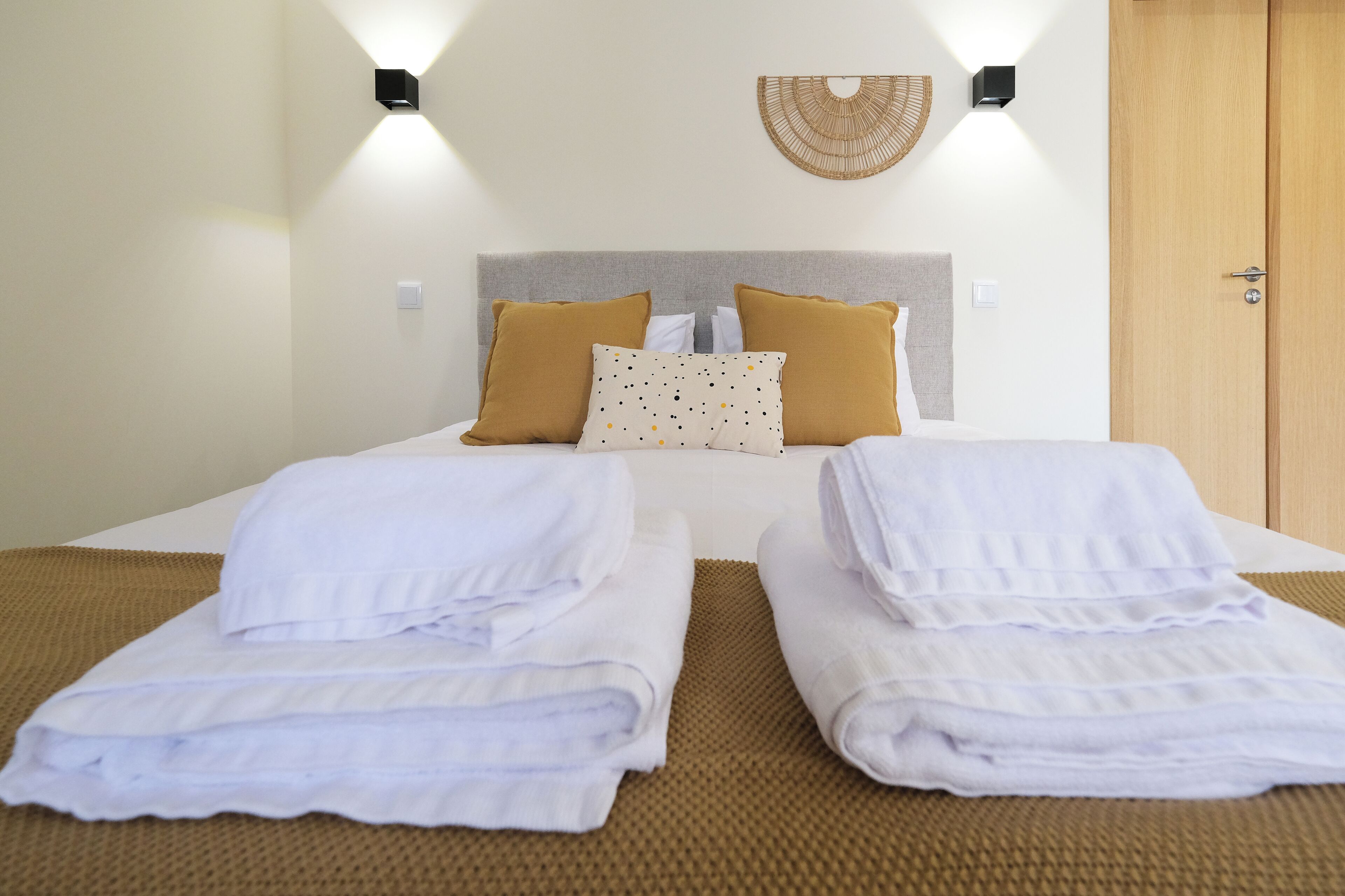 Habitación de hotel con cama, dos almohadas, lámpara de pared y una puerta.