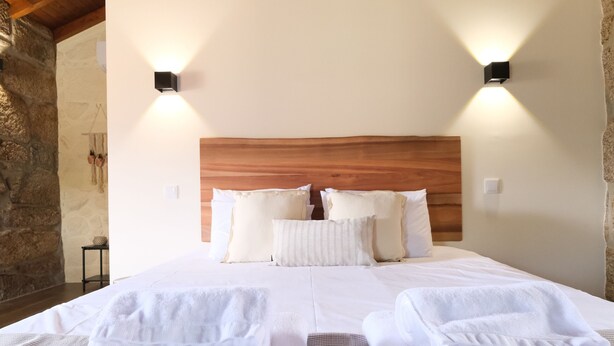 A neatly made bed with white linens and towels, wooden headboard, and two wall-mounted lights. - JADS Guesthouse (Montalegre)