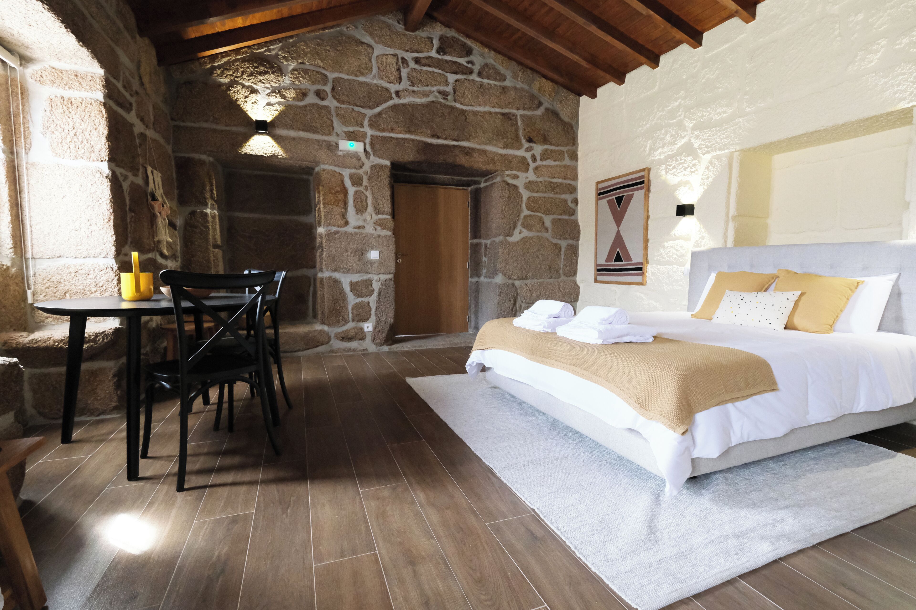 Un dormitorio con cama, una mesa con sillas y una pared de piedra.