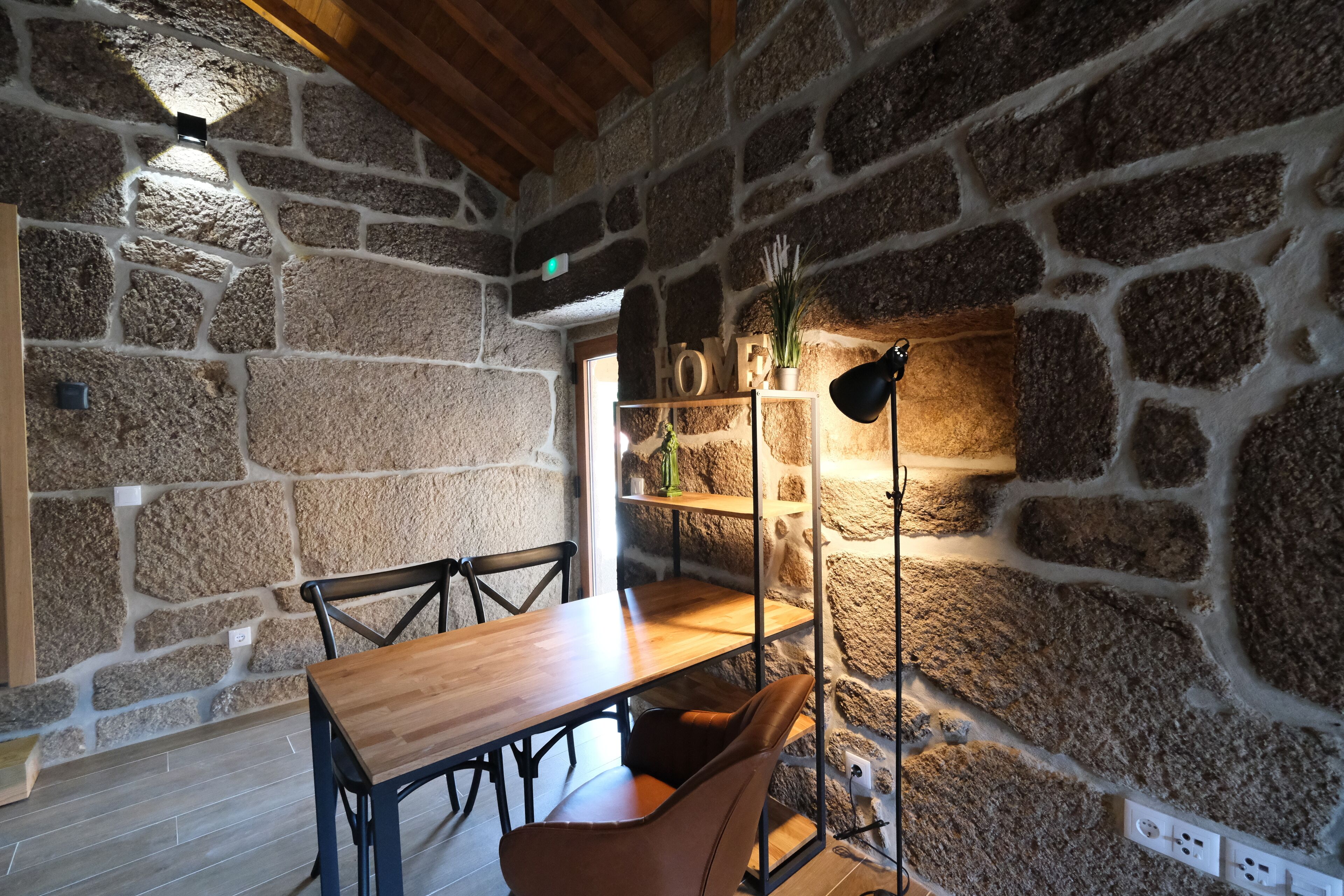 Un intérieur rustique avec un mur en pierre, une table en bois, des chaises et un lampadaire.