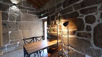 A rustic interior with a stone wall, wooden table, chairs, and a floor lamp.