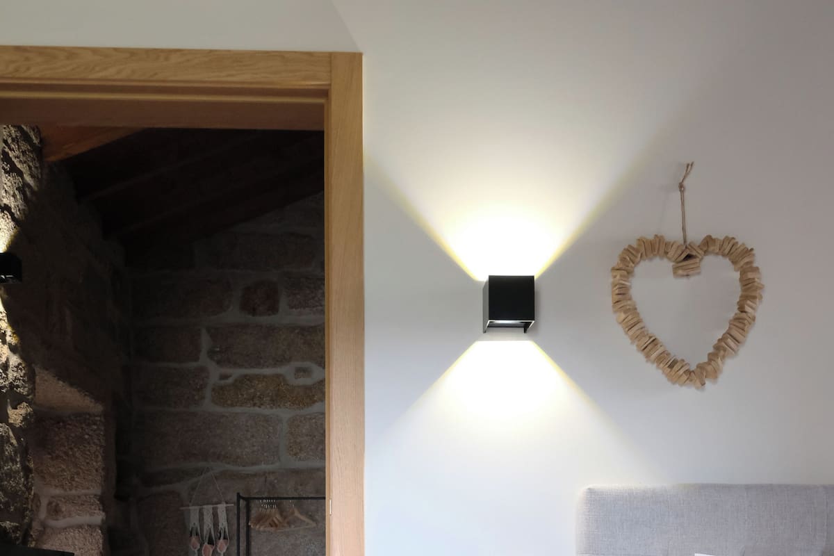 Una camera da letto con parete in pietra, un letto con biancheria bianca, un tavolino rotondo e una decorazione a forma di cuore sulla parete.
