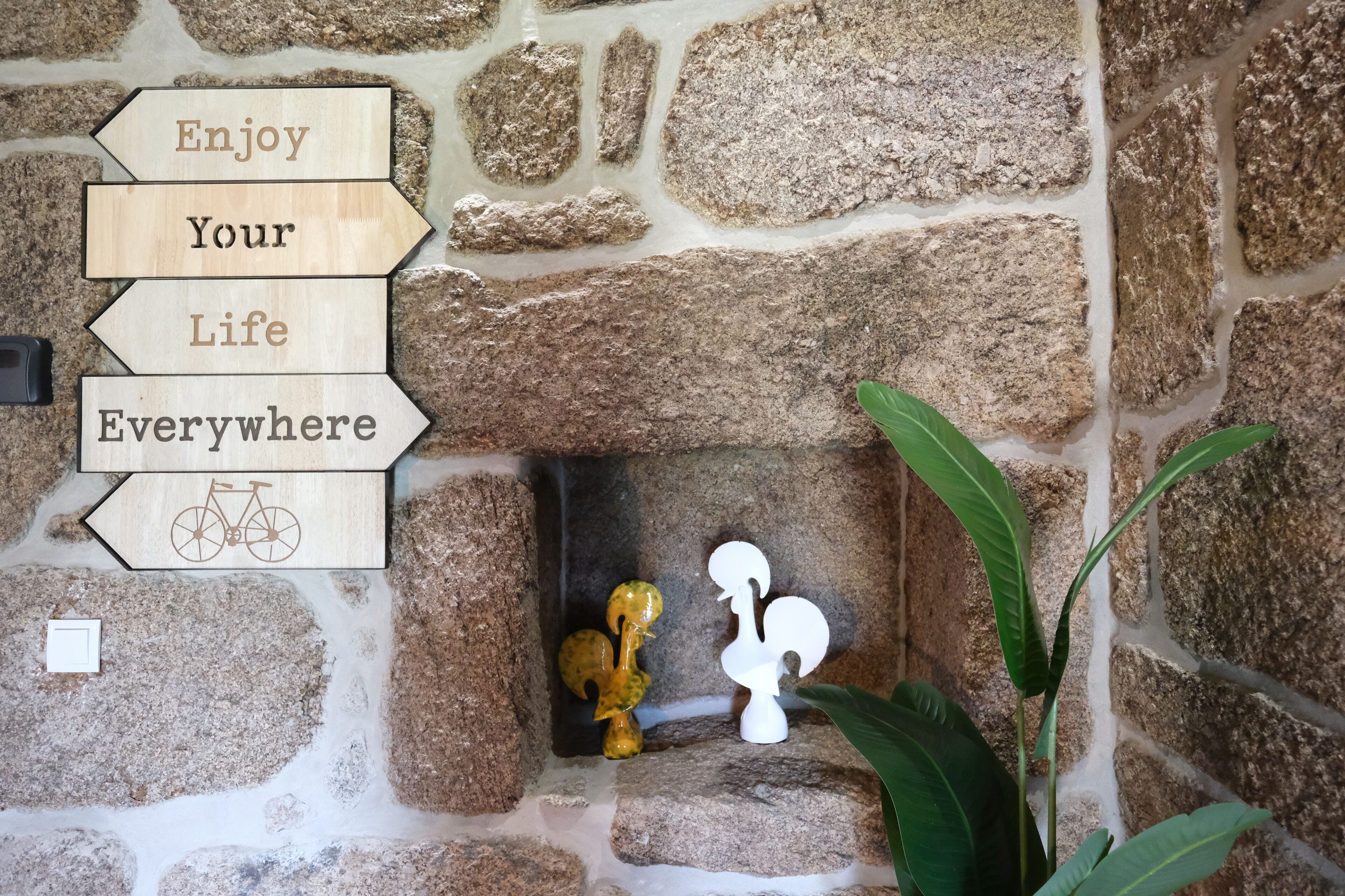 A stone wall with wooden signs that read "Enjoy Your Life Everywhere" and a bicycle symbol.
