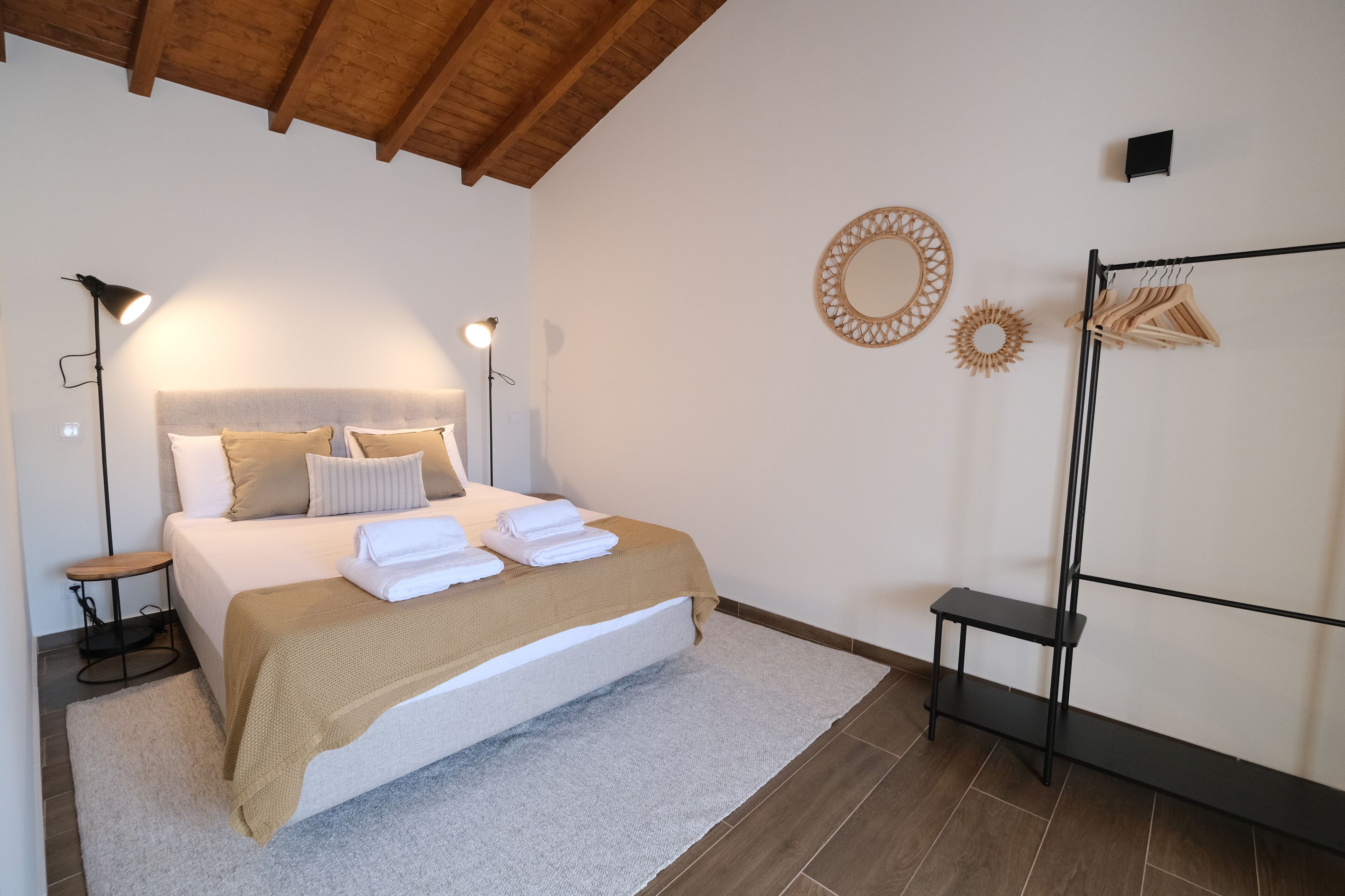 Een opgemaakt bed met witte en beige lakens, een klein nachtkastje en een vloerlamp.