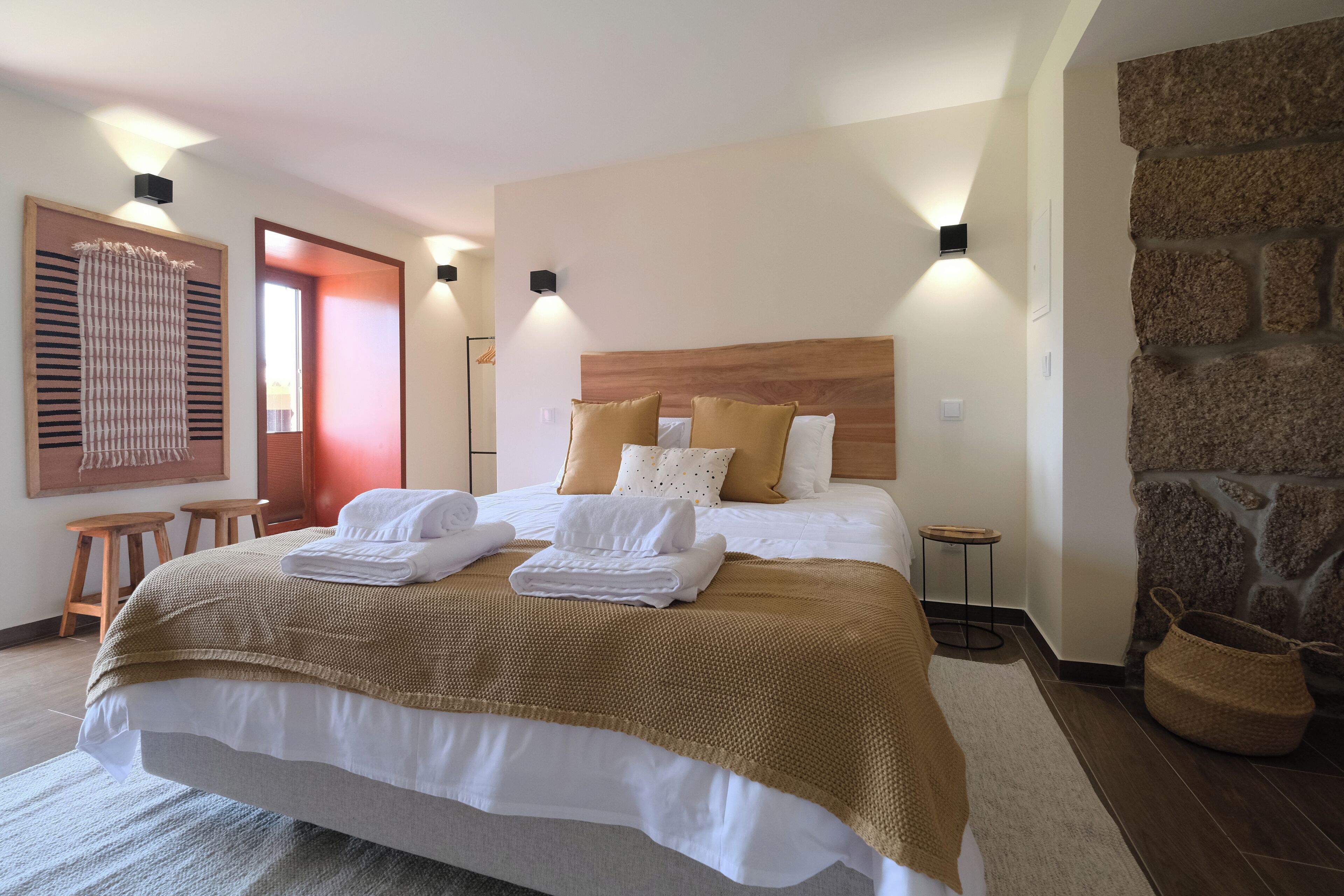 Una cama doble bien hecha con cabecera de madera, dos mesitas de noche y una pared de piedra.