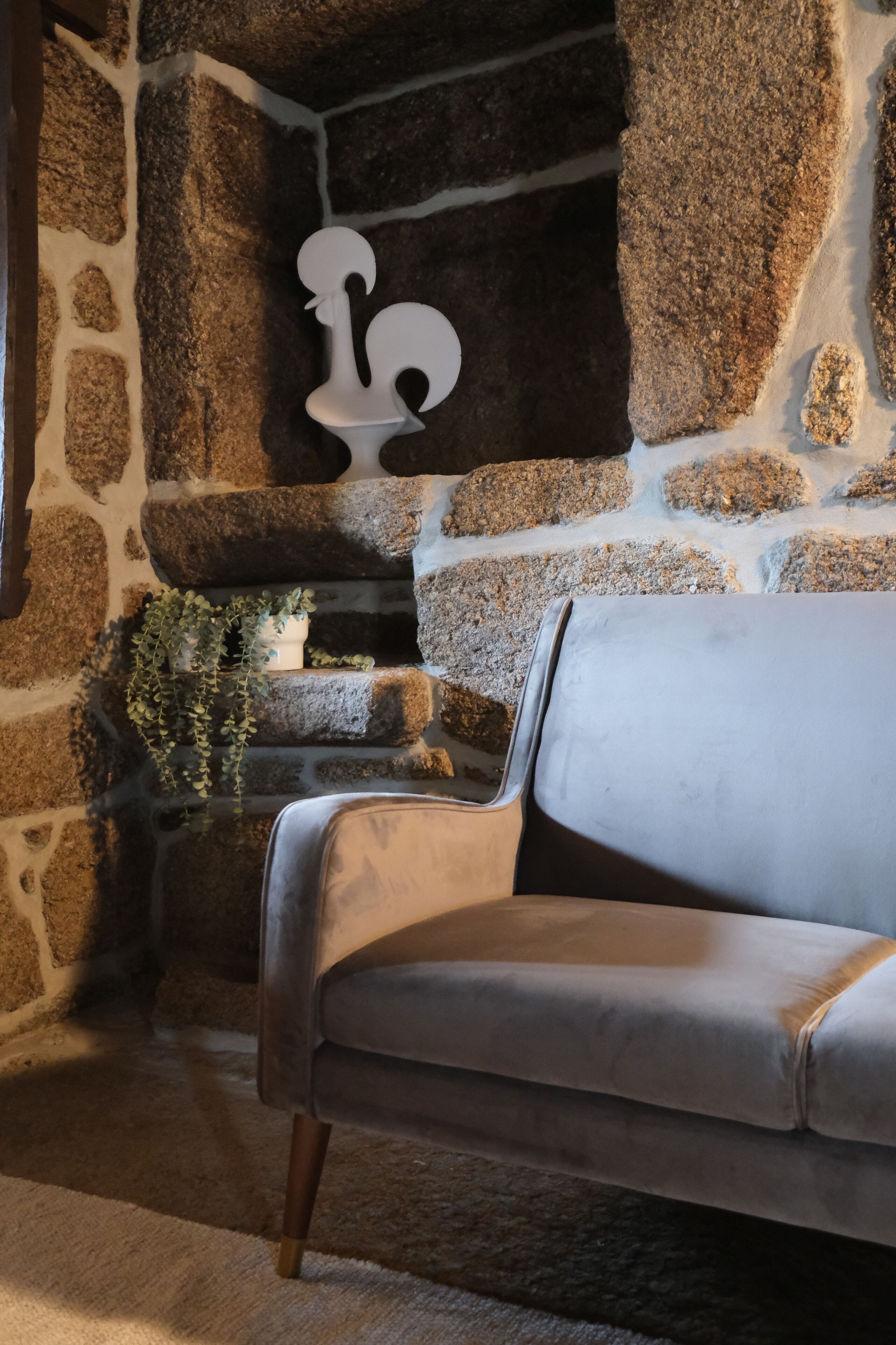 A stone fireplace with a white decorative piece, a gray sofa, and a small plant on a stone ledge.