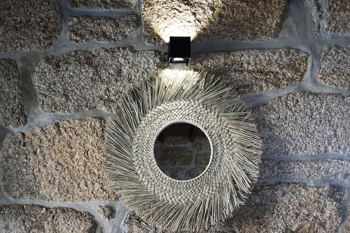 Un muro in pietra con un lampadario circolare intrecciato e due sgabelli di legno.