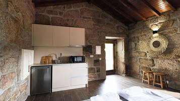 A rustic stone-walled room with a kitchenette, wooden stools, and a bed with white linens.