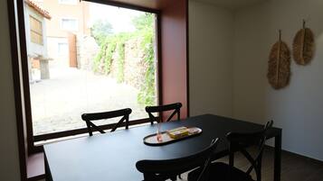 Ein Essbereich mit Tisch und Stühlen, ein Fenster mit Blick auf einen Innenhof und zwei an der Wand befestigte dekorative Blätter.