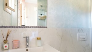 Une salle de bain avec un lavabo blanc, un miroir et un bidet. On peut voir un porte-serviettes et des toilettes.