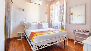 Une chambre à coucher avec un lit, une petite table de chevet, un miroir et une fenêtre avec des rideaux.