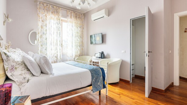 A bedroom with a bed, a bedside table, a chair, a TV, and a door. - Marty Violet - Milù Holidays Firenze
 (Firenze)
