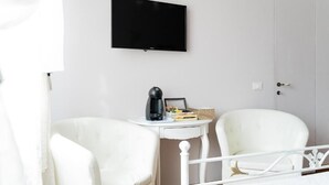 A room with a bed, two white chairs, a small table with a coffee maker, a television on the wall, and a door. - Marty Violet - Milù Holidays Firenze
 (Firenze)