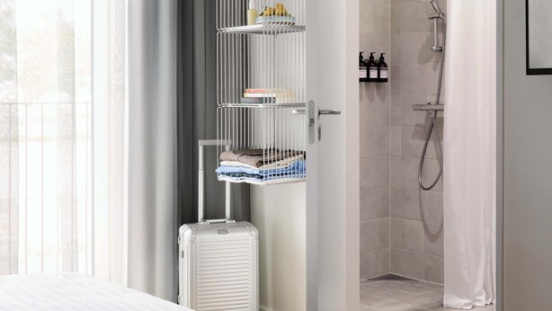 A hotel room with a bed, a white radiator, a storage rack with toiletries, a shower area, and a view of the outdoors. - Studio Apartment for 2 (København)