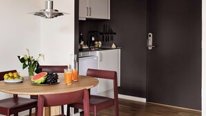 Uma cozinha moderna com armários brancos, uma porta preta e uma área de refeições com mesa de madeira e cadeiras vermelhas.