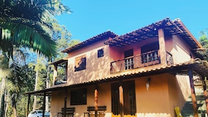 Ein zweistöckiges Haus mit Balkon und überdachter Veranda, davor ein geparktes Auto.