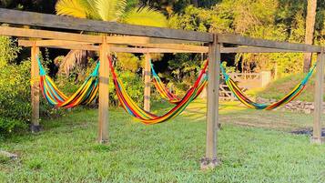 A hammock set up between wooden posts in a grassy area with trees in the background.