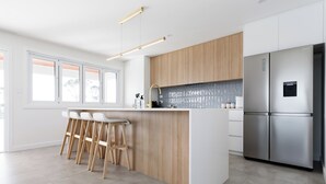 A modern kitchen with a central island, bar stools, a stainless steel refrigerator, and wooden cabinetry. - Spacious 4-Bed Coastal Retreat with Ocean Views (Bridport)