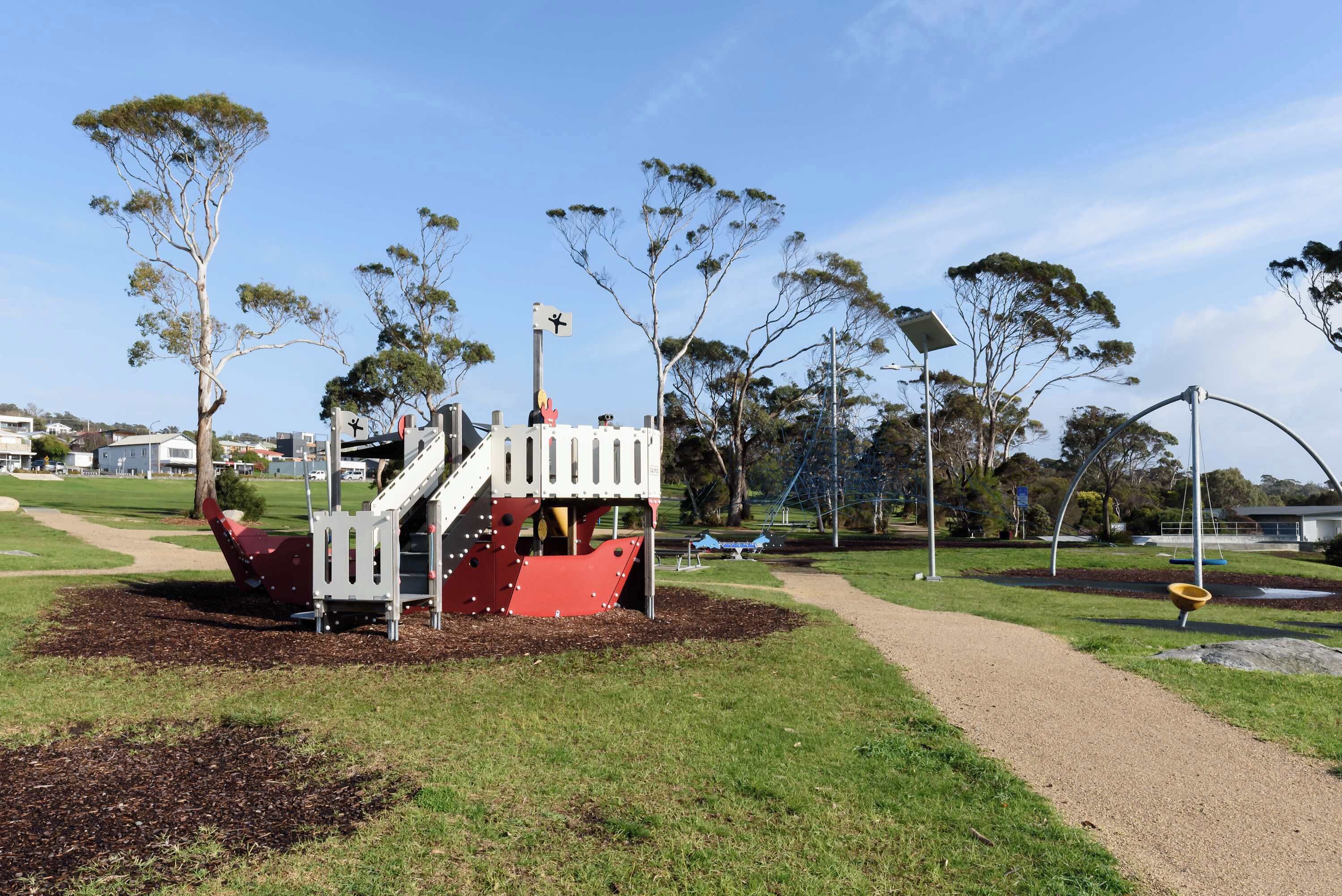 Un parque infantil con un tobogán rojo y una estructura para escalar, rodeado de césped y árboles.