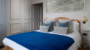 A bedroom with a bed, pillows, a blue bedspread, a wall-mounted painting, and a bedside table with a lamp. - Camellia House, indulge in luxury at our Victorian gem in the heart of Abersoch! (Pwllheli)