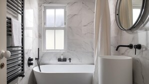A modern bathroom with a freestanding bathtub, a round mirror, and a white sink. - Camellia House, indulge in luxury at our Victorian gem in the heart of Abersoch! (Pwllheli)