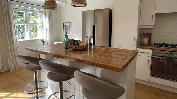 A modern kitchen with a wooden island, bar stools, a refrigerator, and a stove. - Cozy Manchester Hideaway With 2 Bedrooms (Manchester)