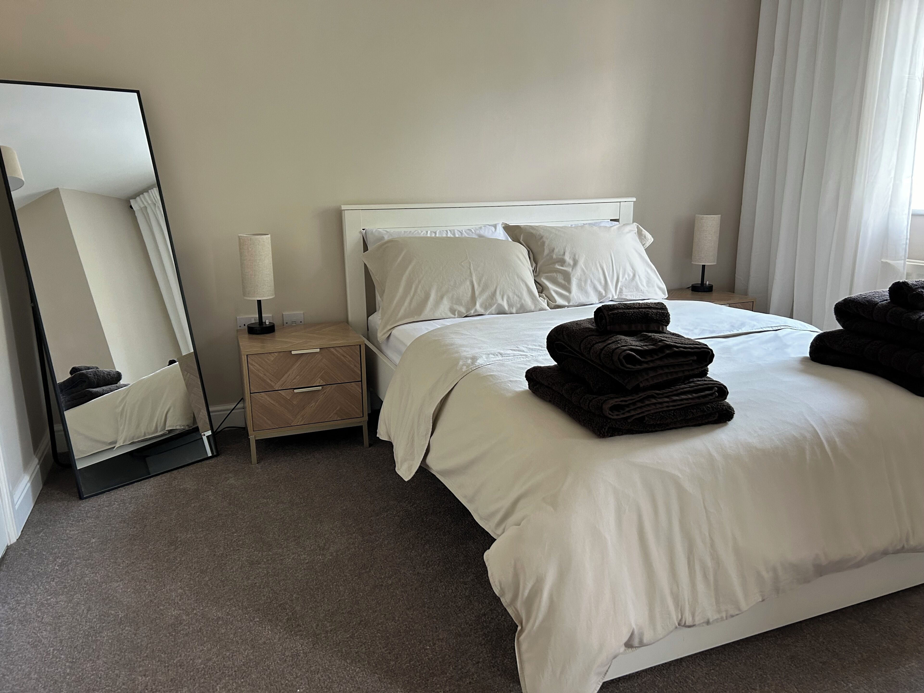 A neatly made bed with white linens, a bedside table with a lamp, and a mirror on the wall.