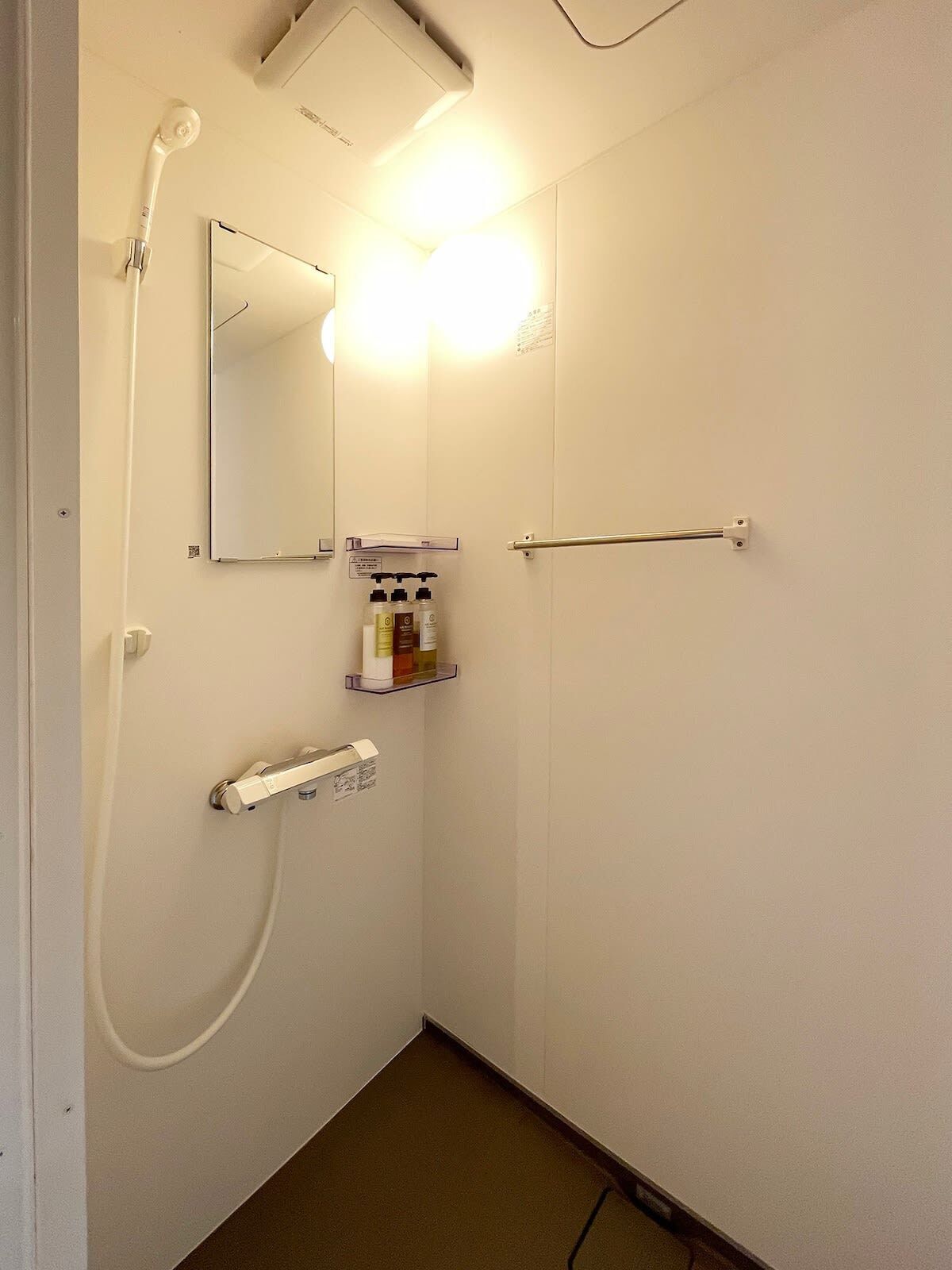 A small, clean bathroom with a shower, a mirror, and a shelf with toiletries.