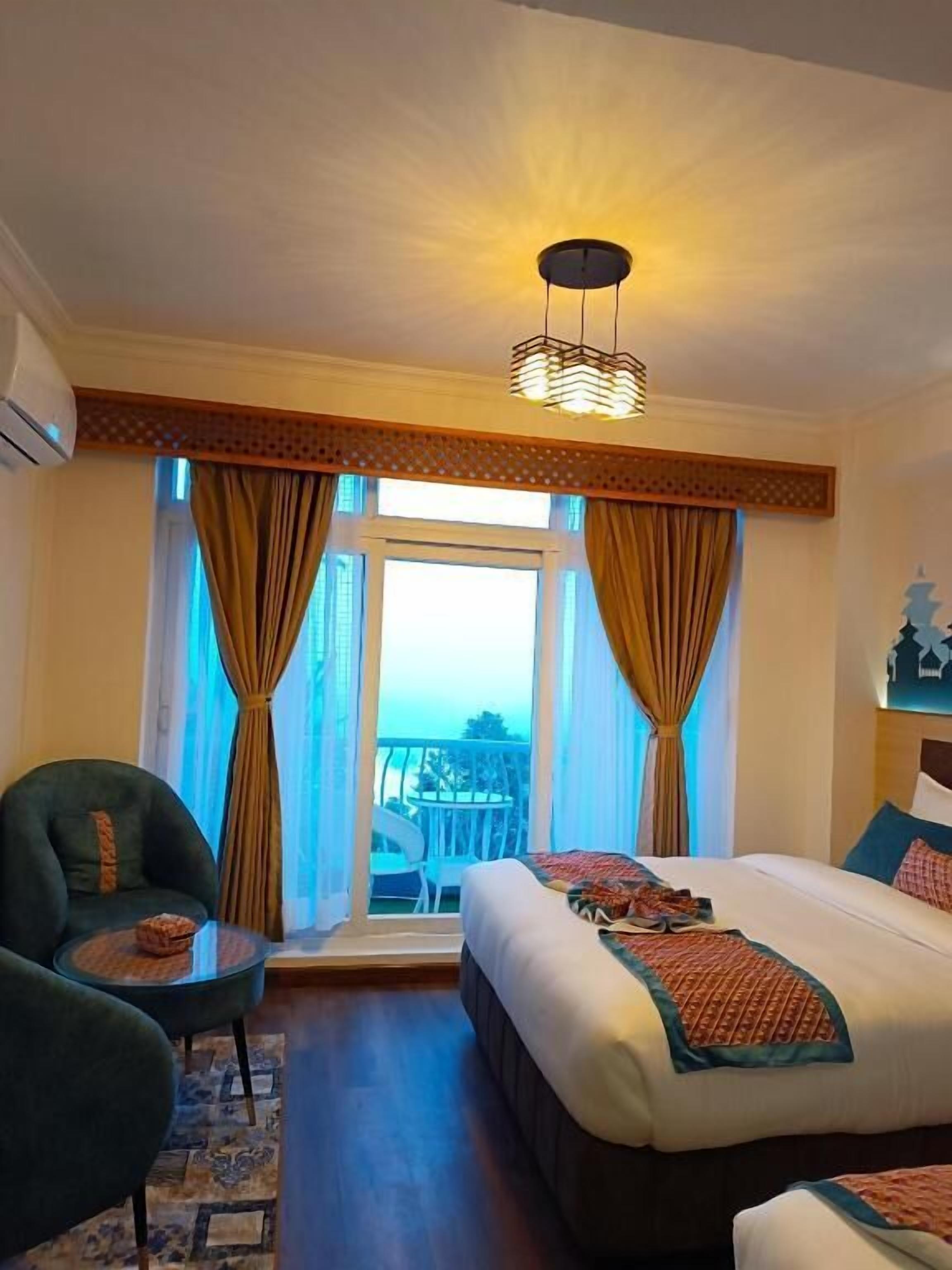 A hotel room with a large bed, a small table, a chair, and a view of the outdoors.