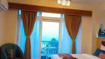 A hotel room with a large bed, a small table, a chair, and a view of the outdoors.