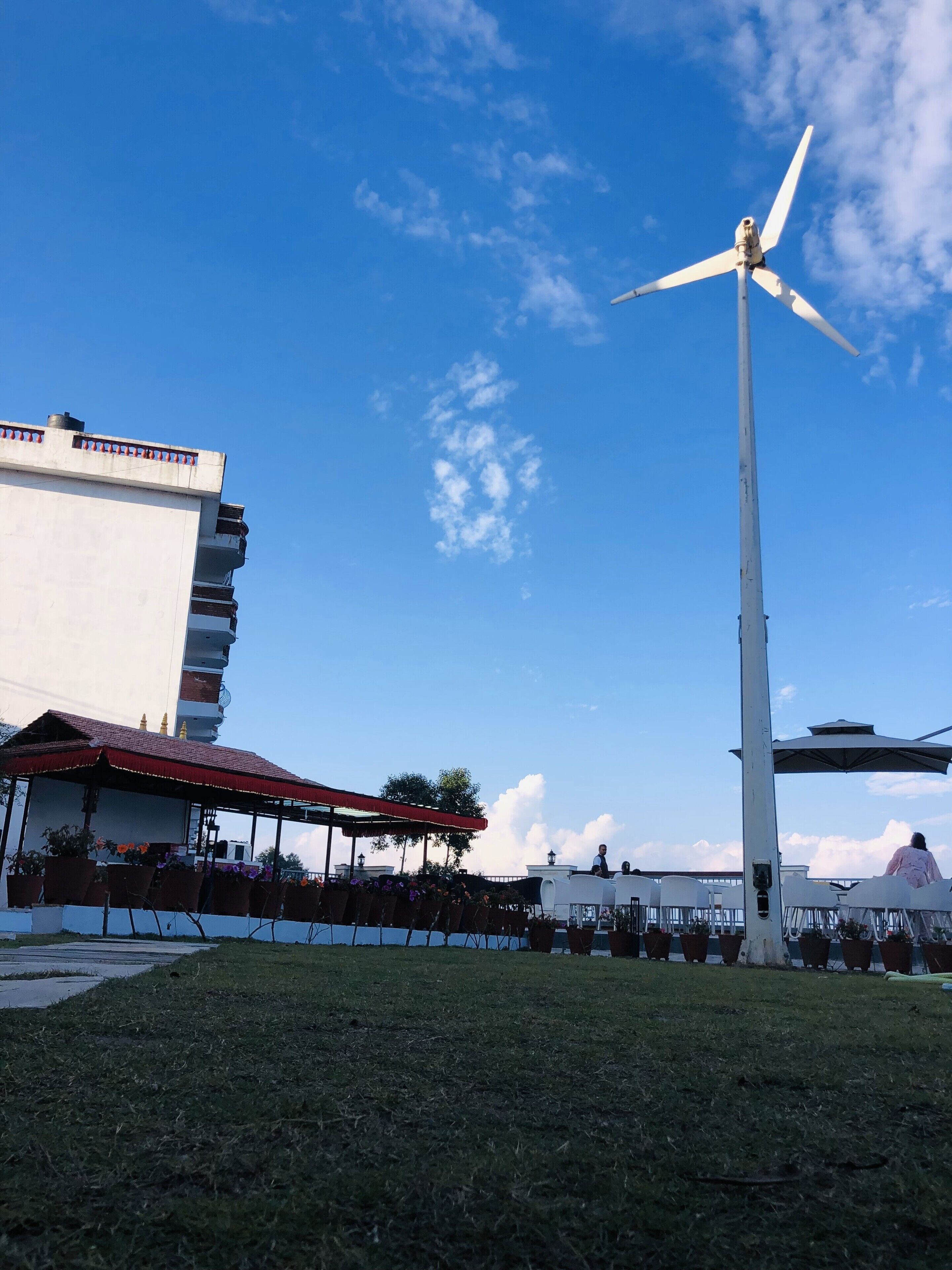 Eine Windkraftanlage, ein Gebäude mit rotem Dach und eine Rasenfläche mit Außenbestuhlung.