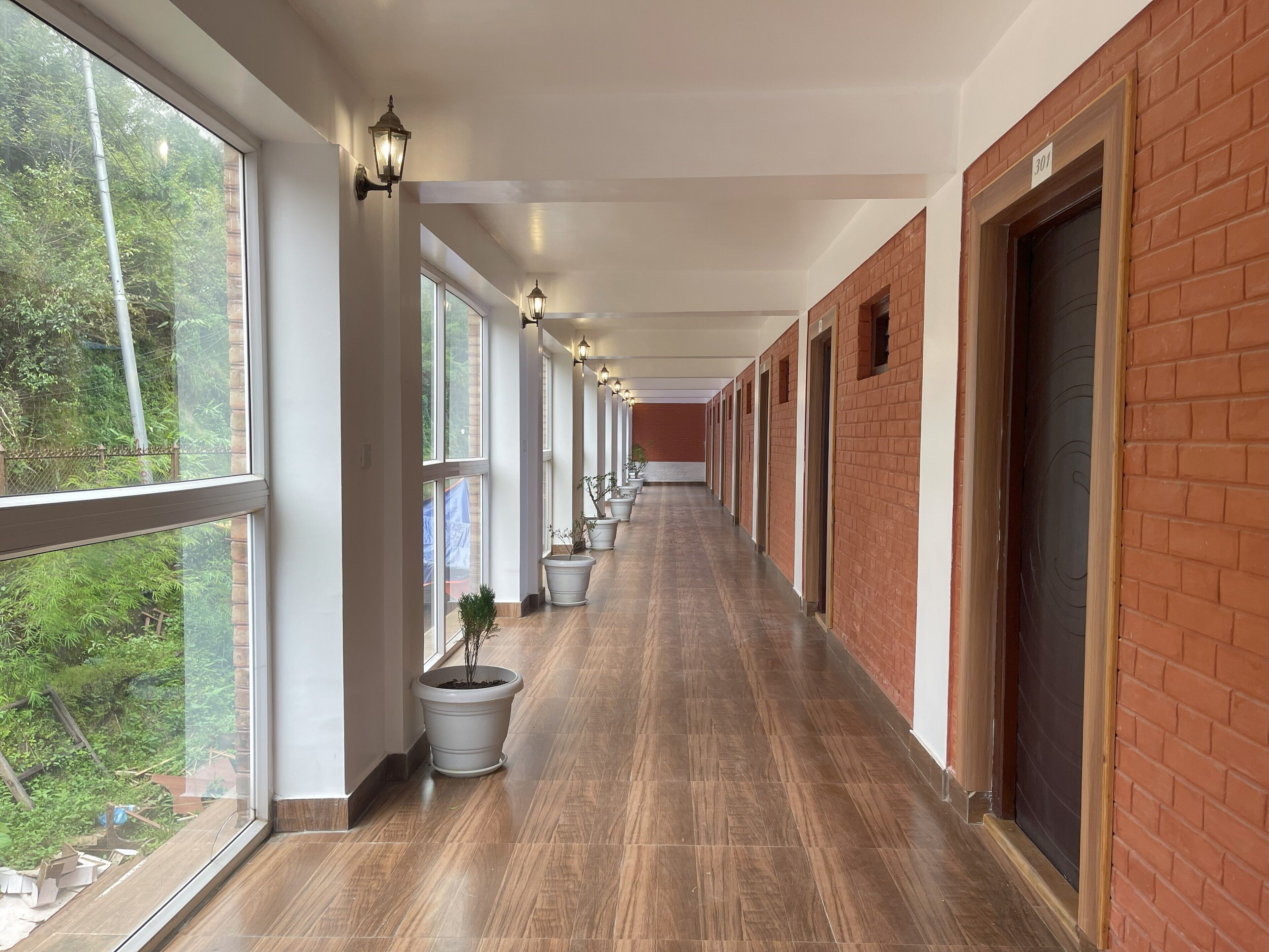 A corridor with large windows, potted plants, and a brick wall.