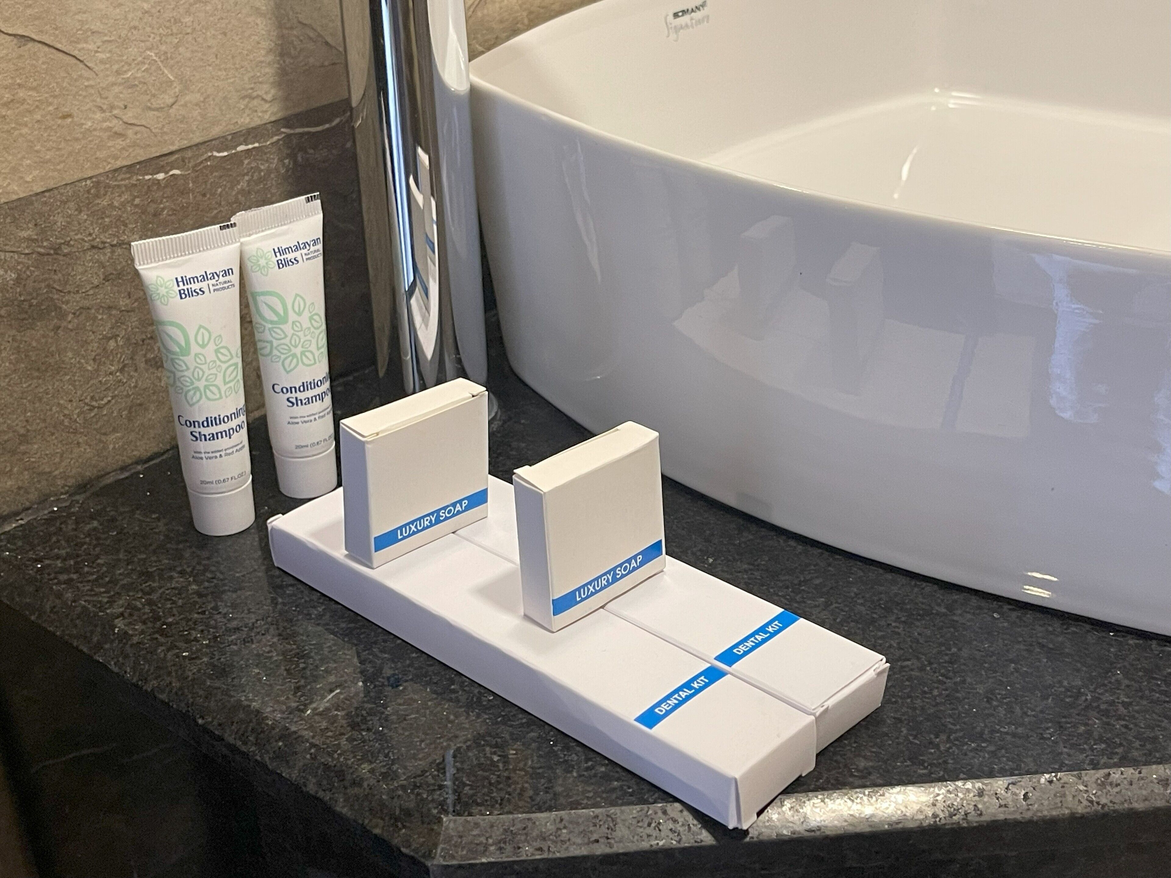 Een badkamermeubel met een groot bad, twee tubes Himalayabliss conditioner, en dozen met de tekst 'Luxe Zeep' en 'Tandenborstelsset'.