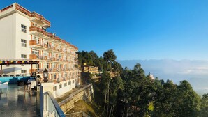 Ein Mehrstöckiges Hotel mit Balkonen, einer Terrasse mit Sitzgelegenheiten und Blick auf die umliegenden Berge und den Wald.