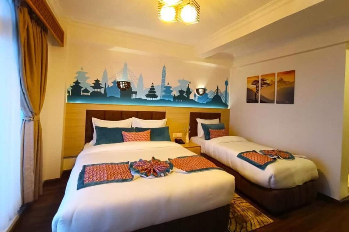 Une chambre d’hôtel avec deux lits, une fresque représentant un paysage urbain sur le mur et un luminaire suspendu.