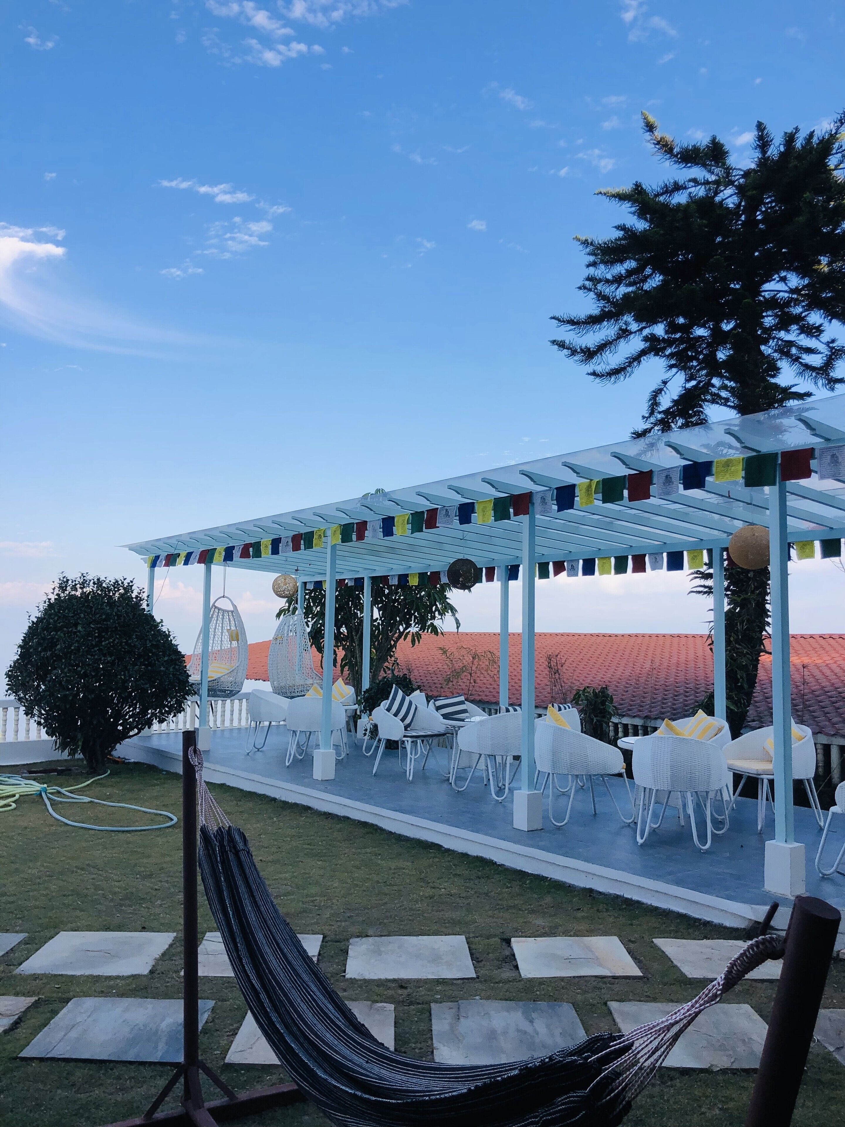 Un espace extérieur aménagé avec des meubles en osier blanc, un hamac et une pergola décorée de fanions colorés.