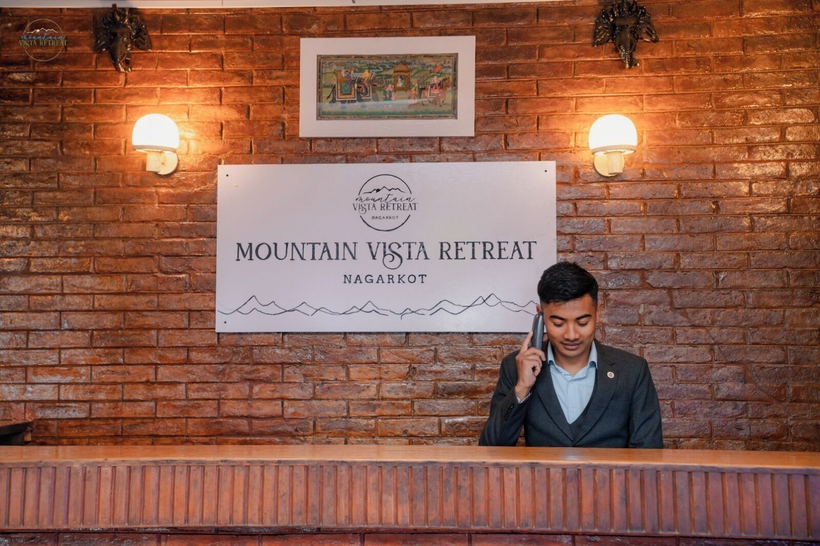 Un comptoir d’accueil à Mountain Vista Retreat, à Nagarkot, avec un panneau indicateur, deux lampes fixées au mur et un tableau encadré au-dessus.