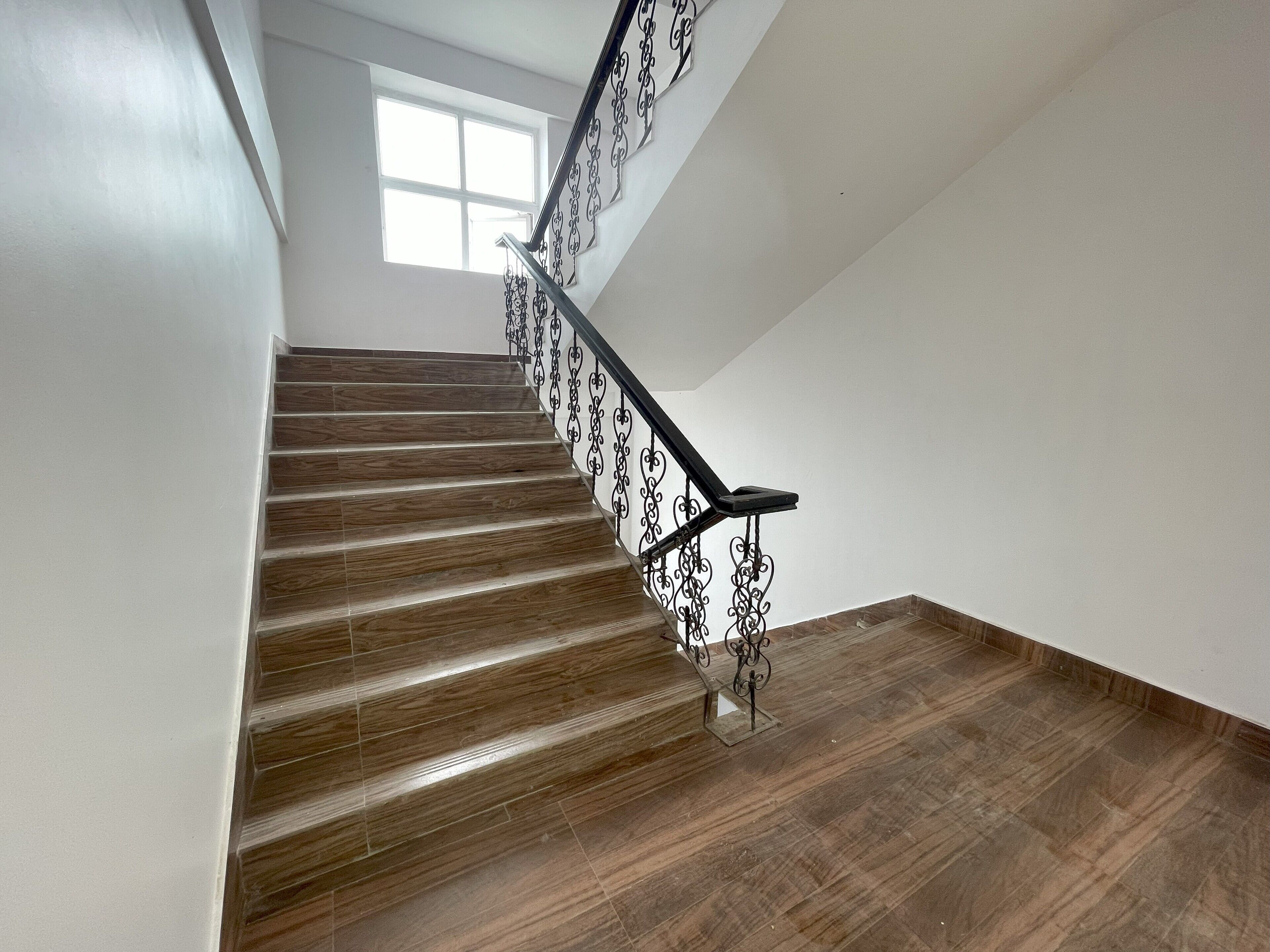 A wooden staircase with black metal railings and a white wall.