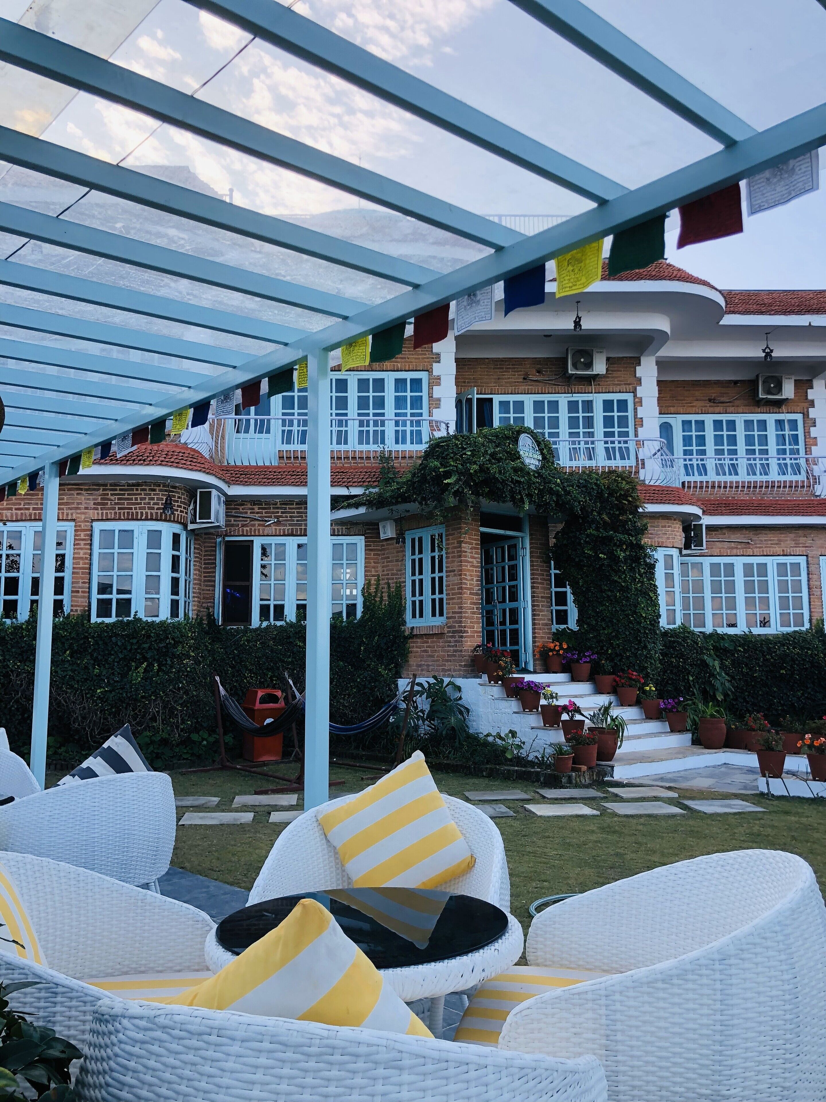A covered outdoor seating area with wicker furniture and a view of a multi-story building with balconies and potted plants.