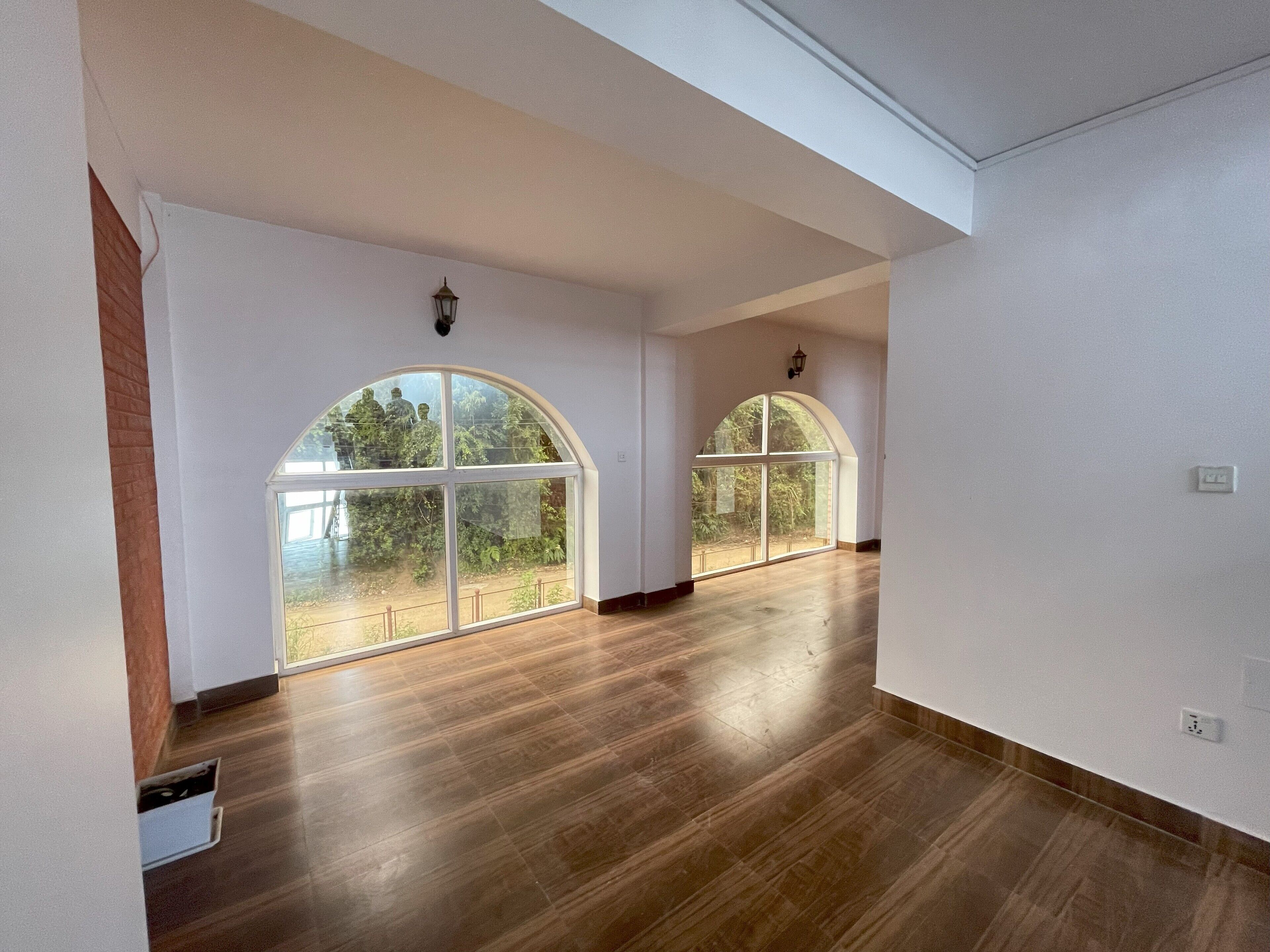 Una habitación amplia con grandes ventanales de arco, suelo de madera y paredes blancas.