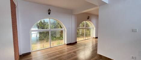 Una habitación amplia con grandes ventanales de arco, suelo de madera y paredes blancas.