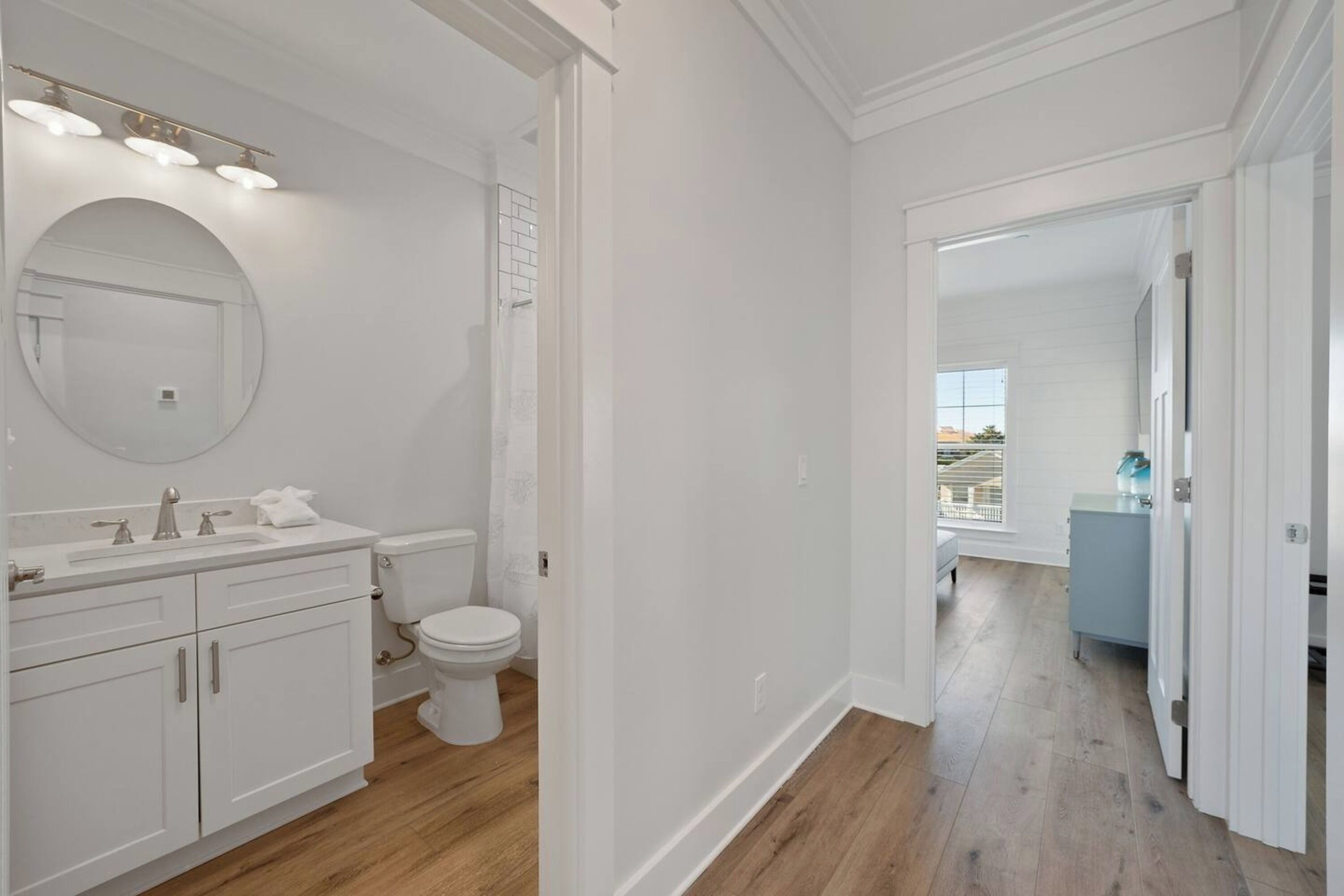 A modern bathroom with white fixtures, a large mirror, and a view to a balcony.
