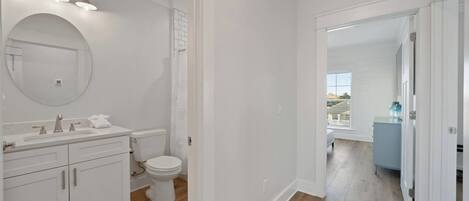 A modern bathroom with white fixtures, a large mirror, and a view to a balcony.